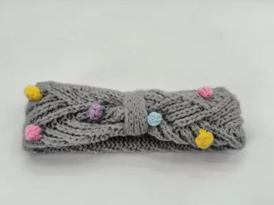 Gestricktes Stirnband in Grau mit Zopfmuster und farbenfrohen Mini-Pompons in Gelb, Rosa, Lila und Blau sowie dekorativem Schleifendetail in der Mitte