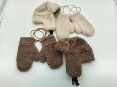 Zwei kuschelige Sherpa-Fleece-Trappermützen mit passenden Fäustlingen in Creme und Braun, durch elastische Halteschnur verbunden, flach auf weißem Hintergrund
