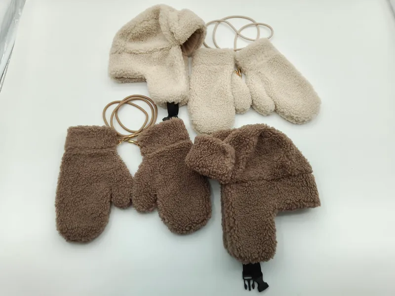 Zwei kuschelige Sherpa-Fleece-Trappermützen mit passenden Fäustlingen in Creme und Braun, durch elastische Halteschnur verbunden, flach auf weißem Hintergrund