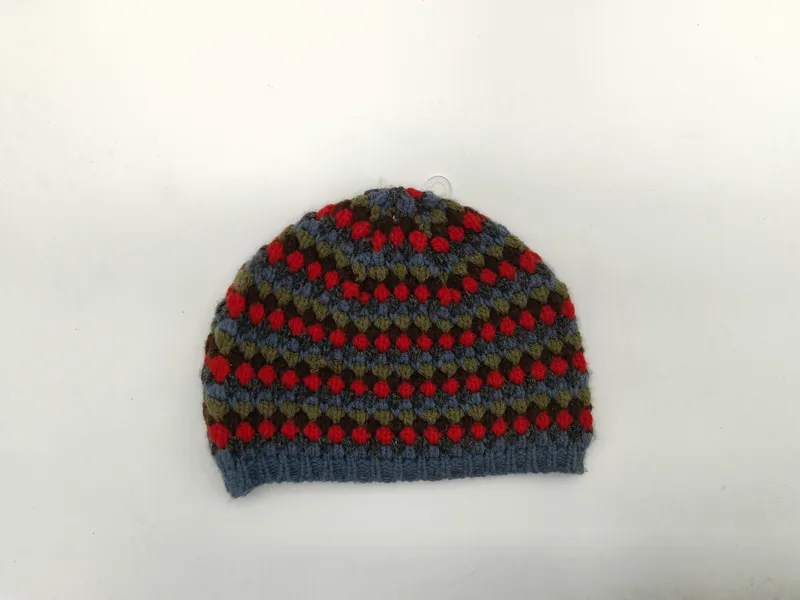 Handgestrickte Bommelmütze mit traditionellem Fair-Isle-Norwegermuster in den Farbtönen Blau, Rot, Olivgrün und Braun auf weißem Hintergrund