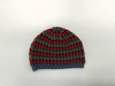 Handgestrickte Bommelmütze mit traditionellem Fair-Isle-Norwegermuster in den Farbtönen Blau, Rot, Olivgrün und Braun auf weißem Hintergrund