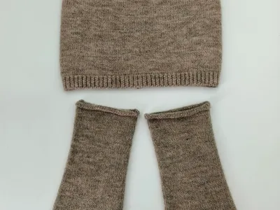 Meliertes Taupe-Beanie und passende fingerlose Strickhandschuhe flach auf weißem Untergrund arrangiert