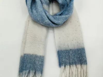 Weicher Winterschal in Blau-Creme-Karomuster mit aufgenähten Zierperlen und Fransenenden, spiralförmig auf hellem Hintergrund drapiert