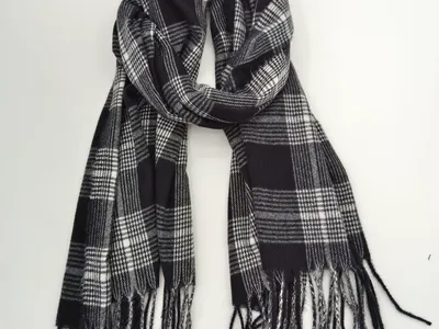 Klassischer Tartan-Schal in Schwarz-Weiß mit geometrischem Karomuster und geknoteten Fransenenden, locker gefaltet auf weißem Untergrund