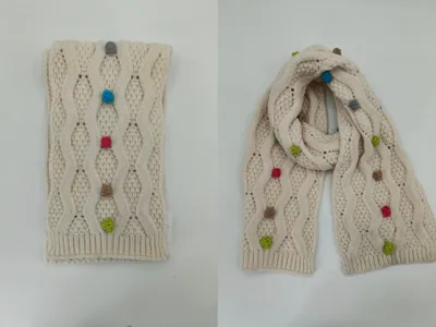 Cremefarbener Wollschal mit Zopfmuster und handgenähten bunten Garnknoten in Blau, Rosa, Grün und Beige, drapiert und gefaltet