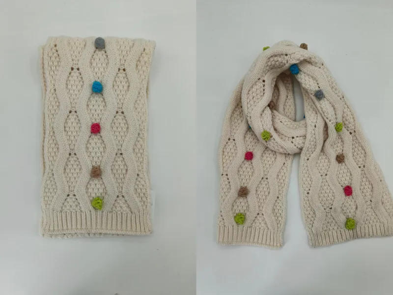 Cremefarbener Wollschal mit Zopfmuster und handgenähten bunten Garnknoten in Blau, Rosa, Grün und Beige, drapiert und gefaltet