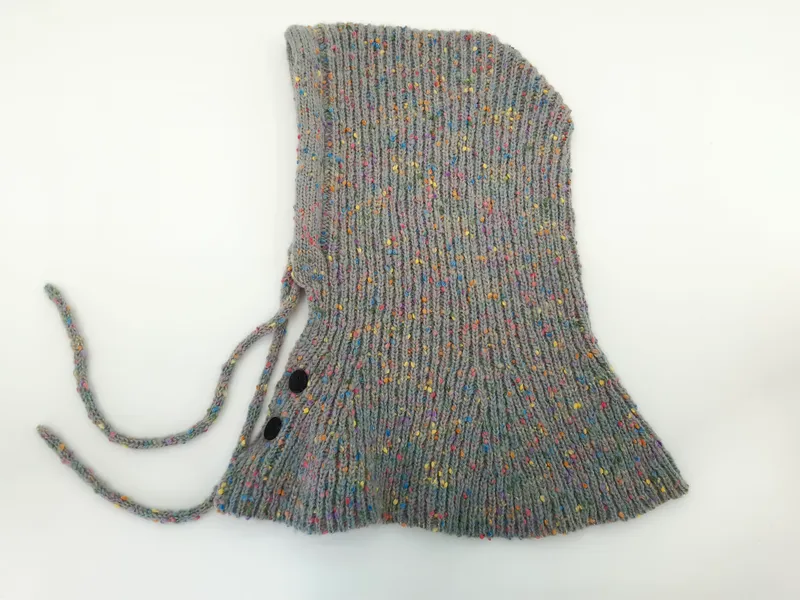 Graue mehrfarbig melierte Strick-Babyhaube mit Kinnbändern und zwei schwarzen Druckknöpfen, als Flachbild auf weißem Hintergrund