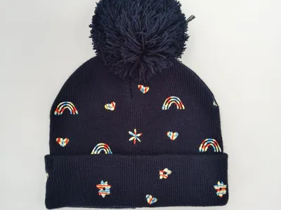 Marine-blaue gerippte Strickmütze mit großem Pompon und bunten gestickten Motiven wie Regenbogen, Herz und Stern