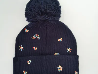 Dunkelblaue gerippte Wintermütze mit flauschigem Pompon und farbigen gestickten Regenbögen, Herzen, Sternen und Blumen