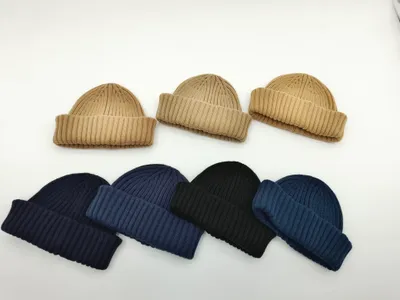 Sieben gerippte Umschlagrand-Beanies in verschiedenen Farbtönen – Beige, Dunkelblau, Schwarz und Blau – auf weißem Hintergrund angeordnet