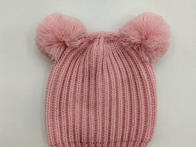 Rosa gerippte Babymütze mit zwei flauschigen Pompons oben, flach auf weißem Hintergrund liegend
