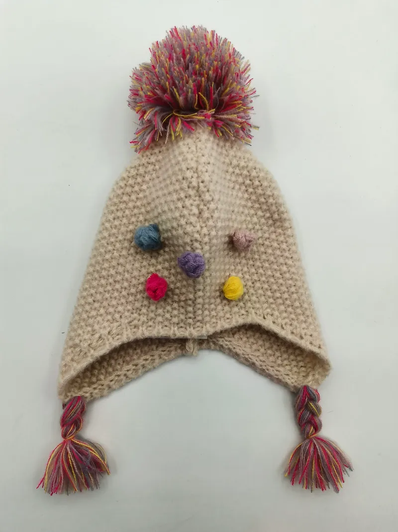 Handgestrickte Creme-Ohrenklappenmütze mit mehrfarbigem Pompon, kleinen bunten Garnbobbles und geflochtenen Quastenbändern mit Fransenden