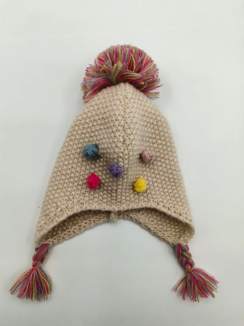 Handgestrickte Creme-Baby-Ohrenklappenmütze mit großem mehrfarbigem Pompon, kleinen bunten Mini-Pompons und geflochtenen Quastenbändern