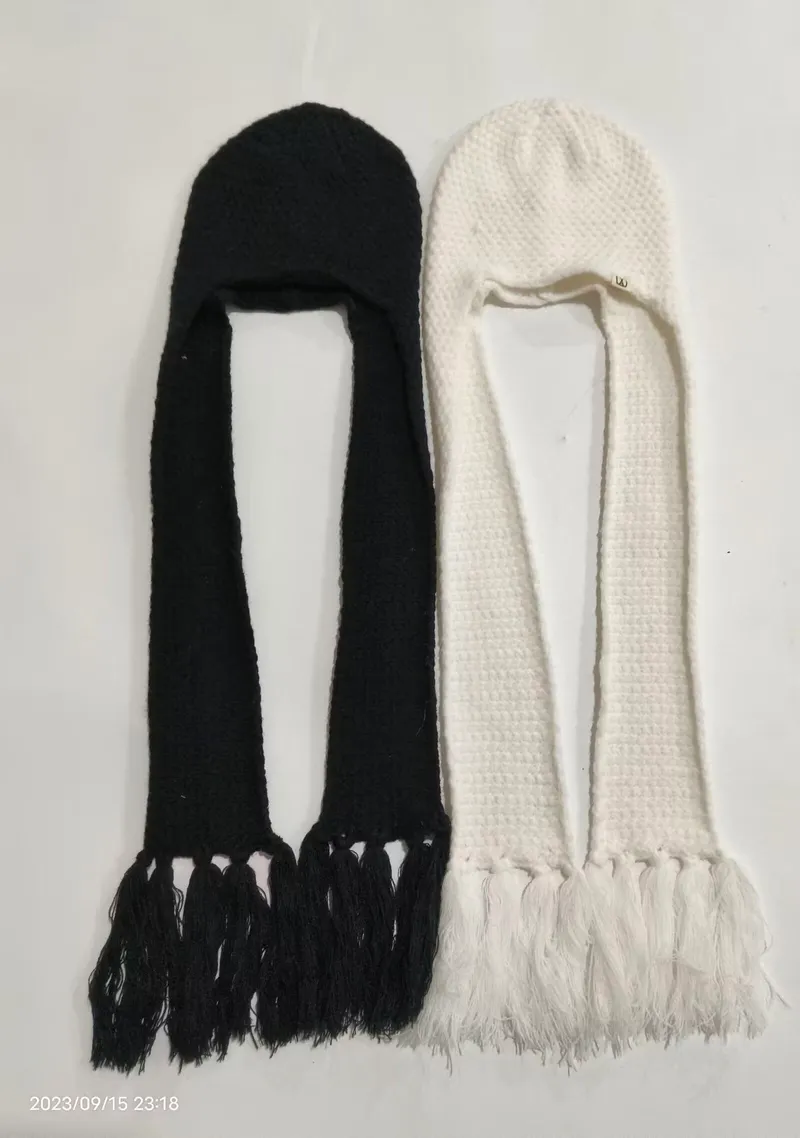 Zwei gestrickte Kapuzenmützen mit langen Quastenenden in Schwarz und Weiß flach liegend, Balaclavastil mit Ohrenschutz
