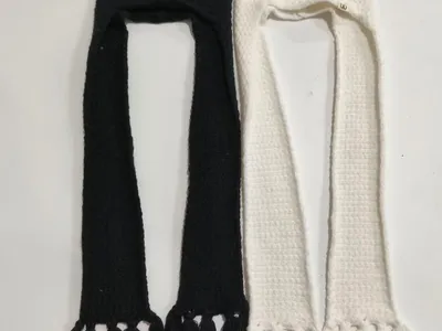 Zwei gestrickte Kapuzenmützen mit langen Quastenenden in Schwarz und Weiß flach liegend, Balaclavastil mit Ohrenschutz
