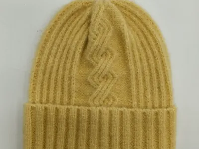 Buttergelbe gerippte Wollstrickmütze mit geometrischem Zopfmustermotiv und breitem Umschlagbündchen, flach auf weißem Hintergrund liegend