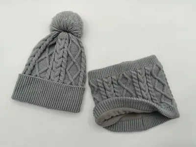 Graue Zopfstrick-Wintermütze mit Bommel und passender Fleece-gefütterter Schlauchschal auf weißem Hintergrund