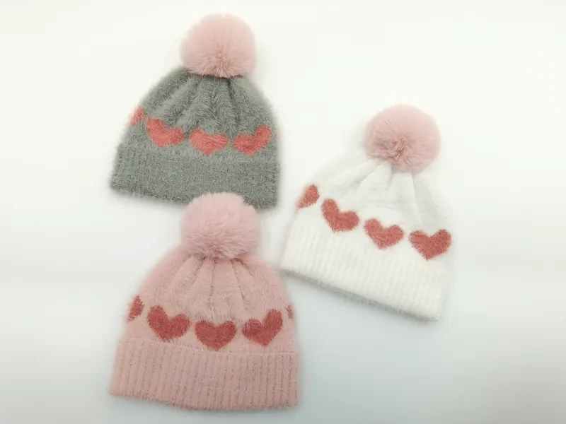 Drei flauschige Strickmützen mit Herz-Jacquard-Muster und Kunstfell-Pompon in Grau, Rosa und Weiß