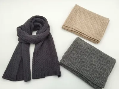 Drei Zopfstrickschals in Anthrazit, Hellgrau und Beige – einer offen drapiert, zwei gefaltet, auf weißem Untergrund