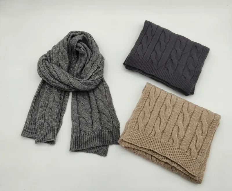 Drei Zopfstrickschals in Grau, Dunkelanthrazit und Beige, gefaltet und flach auf weißem Hintergrund präsentiert