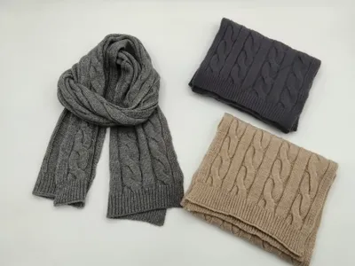 Drei Zopfstrickschals in Grau, Dunkelanthrazit und Beige, gefaltet und flach auf weißem Hintergrund präsentiert