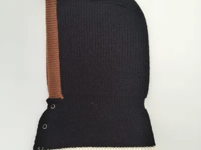 Schwarze Rippenstrick-Balaclava mit braunem Rand, cremefarbenem Streifenakzent und silbernen Druckknöpfen, freigestellt auf weißem Hintergrund