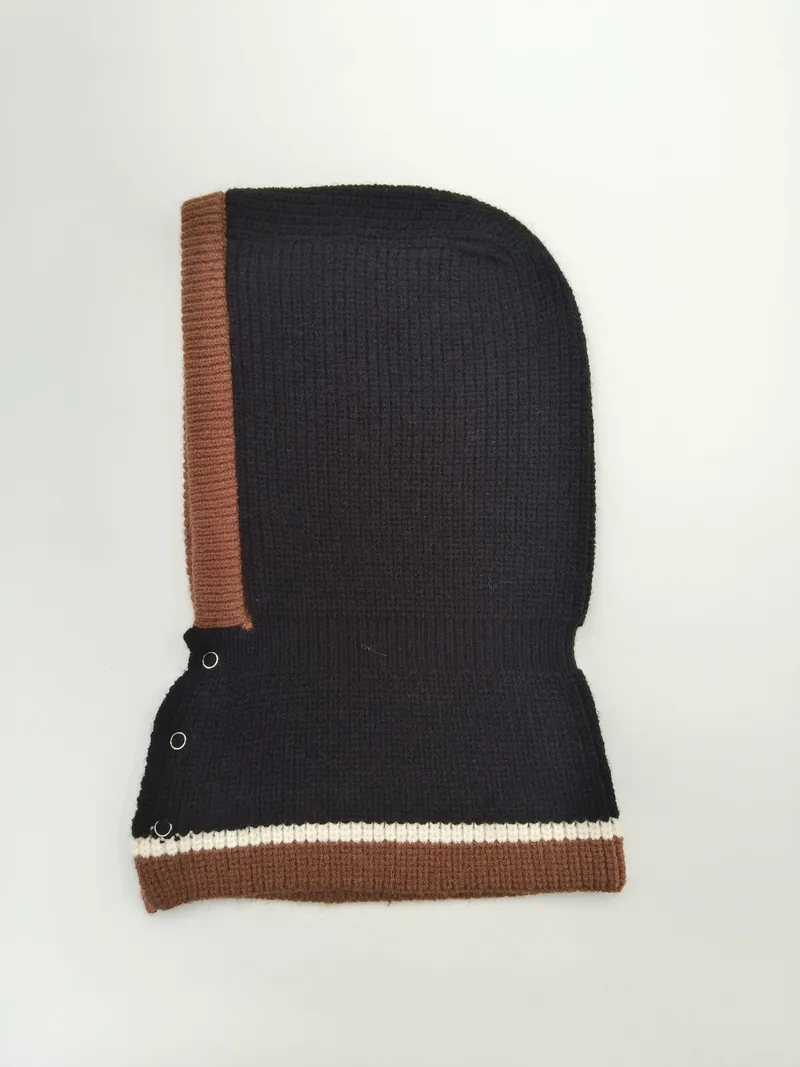 Schwarze Rippenstrick-Balaclava mit braunem Rand, cremefarbenem Streifenakzent und silbernen Druckknöpfen, freigestellt auf weißem Hintergrund