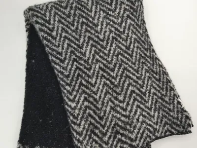 Gefalteter schwarz-grauer Strickschal mit Chevron-Zickzack-Muster und flauschiger Wollmischungs-Textur auf weißem Hintergrund