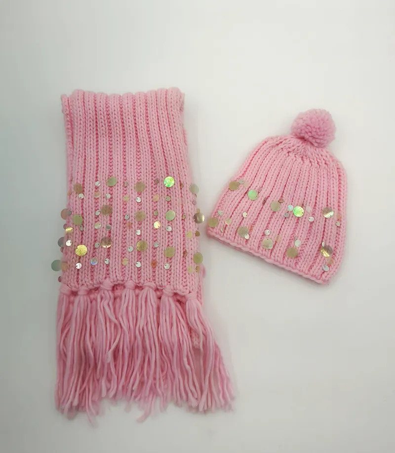 Pinker Rippenstrick-Winterschal mit Fransen und Pailletten, kombiniert mit passender Bommelmütze auf weißem Hintergrund
