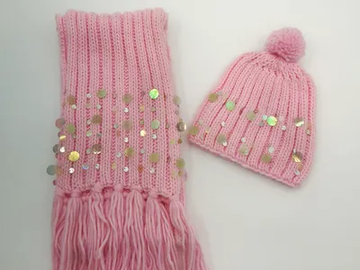 Pinker Rippenstrick-Winterschal mit Fransen und Pailletten, kombiniert mit passender Bommelmütze auf weißem Hintergrund