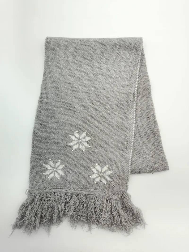 Gefaltete graue Strickdecke mit eingestrickten weißen Schneeflockenmotiven und Fransensaum auf weißem Untergrund