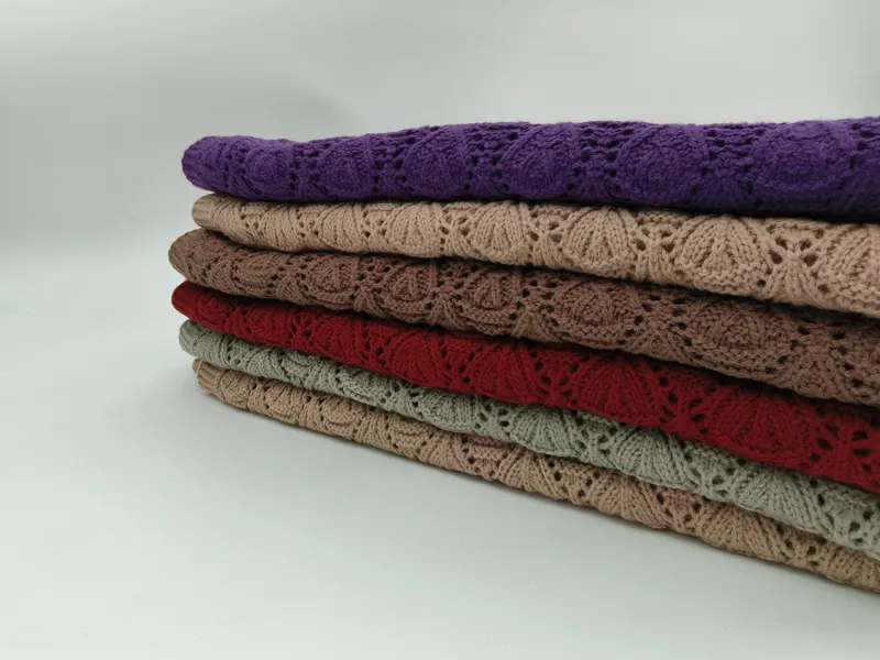 Sechs übereinandergestapelte gefaltete Strickdecken mit floralem Lochmuster in Lila, Beige, Taupe, Rot, Salbeigrün und Hellbraun