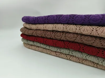 Sechs übereinandergestapelte gefaltete Strickdecken mit floralem Lochmuster in Lila, Beige, Taupe, Rot, Salbeigrün und Hellbraun