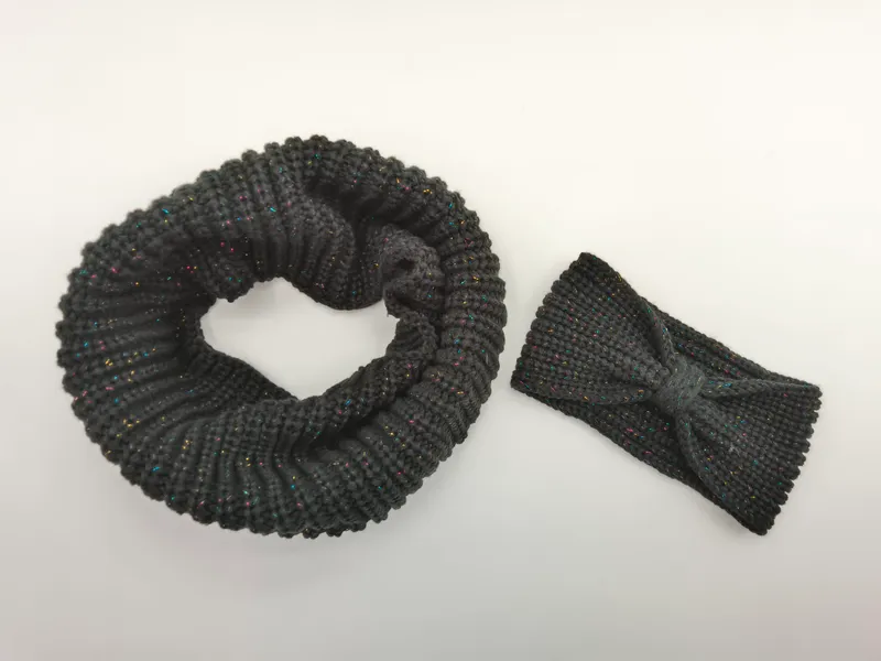 Dunkelgrauer Infinity-Schal aus Grobstrick neben passendem Schleifenhaarband mit farbigen Metallic-Lurexfäden auf weißem Hintergrund