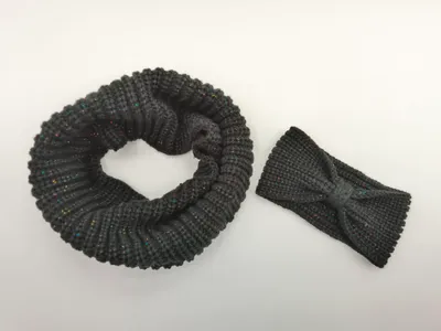 Dunkelgrauer Infinity-Schal aus Grobstrick neben passendem Schleifenhaarband mit farbigen Metallic-Lurexfäden auf weißem Hintergrund
