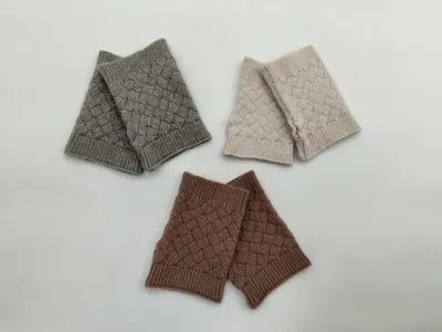 Drei Paar fingerlose Handschuhe mit Korbflechtmuster in den Farben Grau, Cremeweiß und Braun, flach auf weißem Untergrund angeordnet