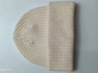 Cremeweiße Rippenstrickmütze mit umgeschlagenem Bündchen auf weißer Fläche, klassische Stricktextur in Naturweiß