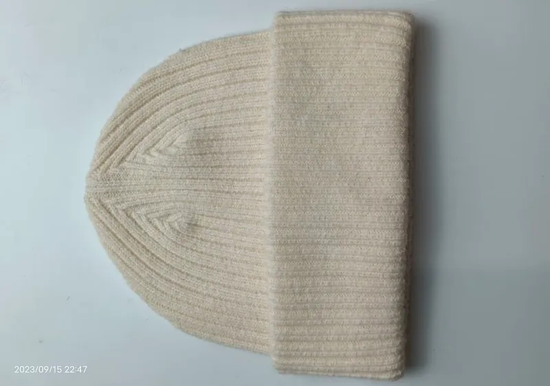 Cremeweiße Rippenstrickmütze mit umgeschlagenem Bündchen auf weißer Fläche, klassische Stricktextur in Naturweiß