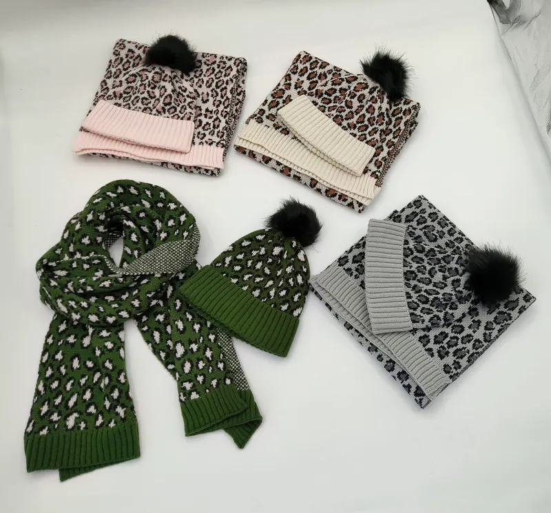 Vier Leopardenmuster-Mützen-und-Schal-Sets in Pink, Creme, Grün und Grau mit schwarzen Kunstfell-Pompons, auf weißer Fläche präsentiert