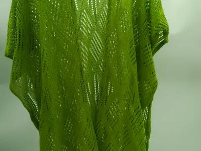 Limettengrüner Häkel-Kimono mit Rauten-Chevron-Muster auf schwarzem Kleiderbügel vor weißer Wand