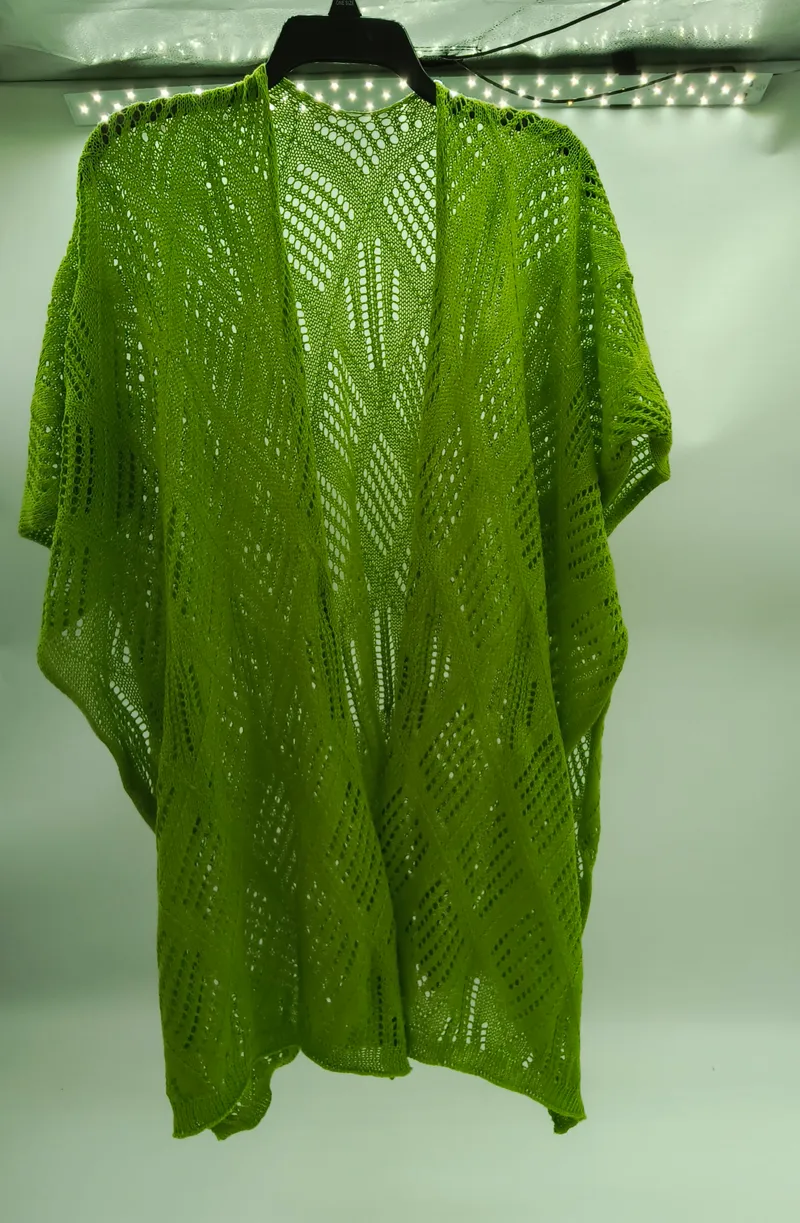 Limettengrüner Häkel-Kimono mit Rauten-Chevron-Muster auf schwarzem Kleiderbügel vor weißer Wand