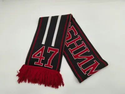 Schwarzer Strick-Fanschal mit rot-weißen Streifen, Nummer 47, Großbuchstaben-Schriftzug und roten Fransentroddeln auf weißem Hintergrund