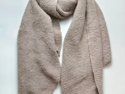 Beiger Rippenstrickschal locker drapiert auf weißem Untergrund, sichtbare weiche Streifenstruktur im Strickmuster