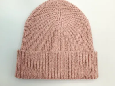 Strickmütze in gedämpftem Rosaton mit breitem gefaltetem Bündchen auf weißem Hintergrund, flach fotografiert