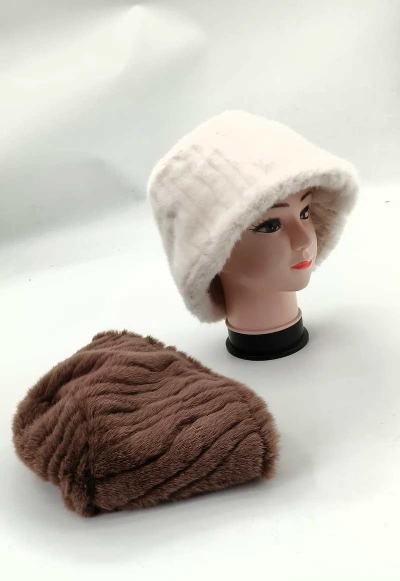 Weißer Kunstfell-Bucket-Hat auf Schaufensterkopf neben flach liegender brauner Plüschmütze auf weißer Fläche