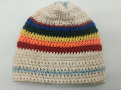 Handgestrickte Cremeweiß-Mütze mit Regenbogenstreifen in Rot, Orange, Gelb, Grün und Blau auf offenem Maschennetz-Untergrund