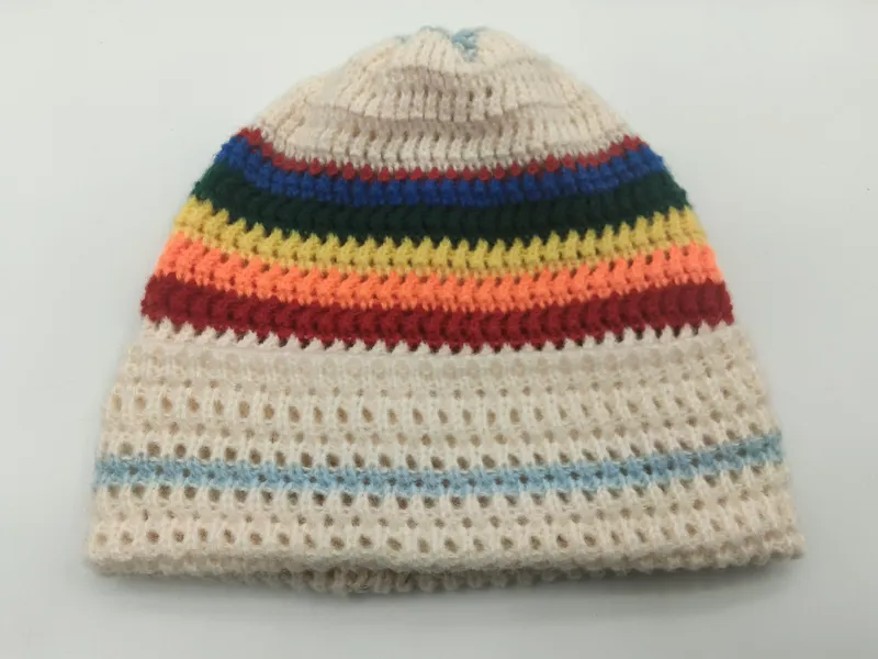 Gestrickte Mütze in Cremefarben mit bunten Streifen in Rot, Orange, Gelb, Grün und Blau sowie offenem Netzmuster am Körper