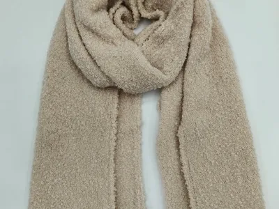 Großformatiger Bouclé-Strickschal in warmem Beige, locker drapiert auf weißem Untergrund