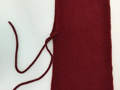 Weinrote gestrickte Sturmhaube mit feinem Rippenmuster und langen Schnürbändern, von oben fotografiert auf hellem Untergrund