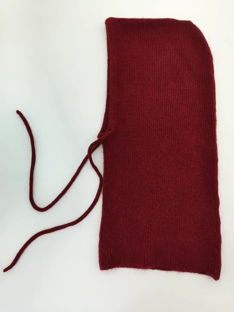 Weinrote gestrickte Sturmhaube mit feinem Rippenmuster und langen Schnürbändern, von oben fotografiert auf hellem Untergrund